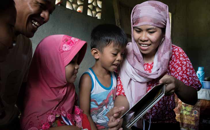 ​ Jenaica, 4, (pink headscarf), and her family read together at home, in Mindanao, Philippines. © SavetheChildren/Hannah Adcock