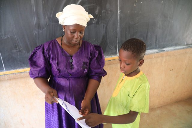 Awa Warma, a teacher in Mopti who is integrating play-based learning to support the literacy of her grade 4 students. She is shown demonstrating an exercise with a student. 